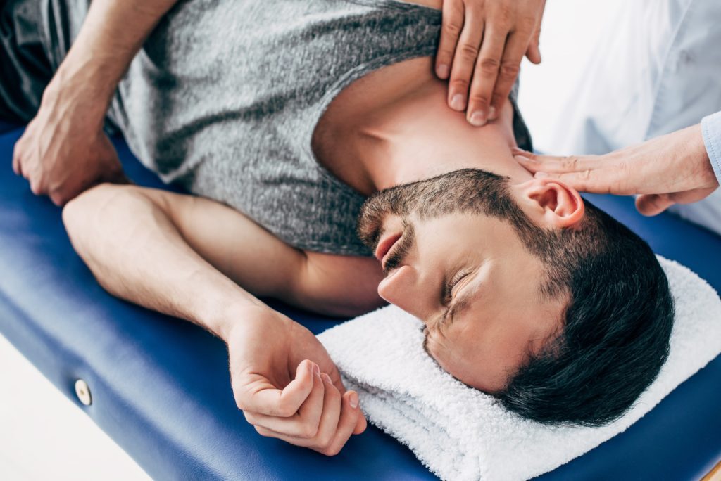 chiropractor massaging neck of man lying on Massage Table