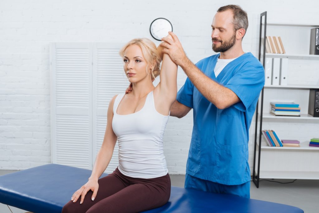 smiling chiropractor stretching womans arm on massage table in clinic